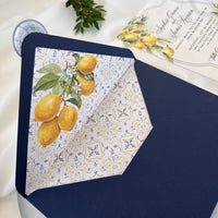 Luxury transparent acrylic wedding invitation with citrus print, blue envelope with tile and lemon insert, completed with a blue wax seal reading “WE DO.”