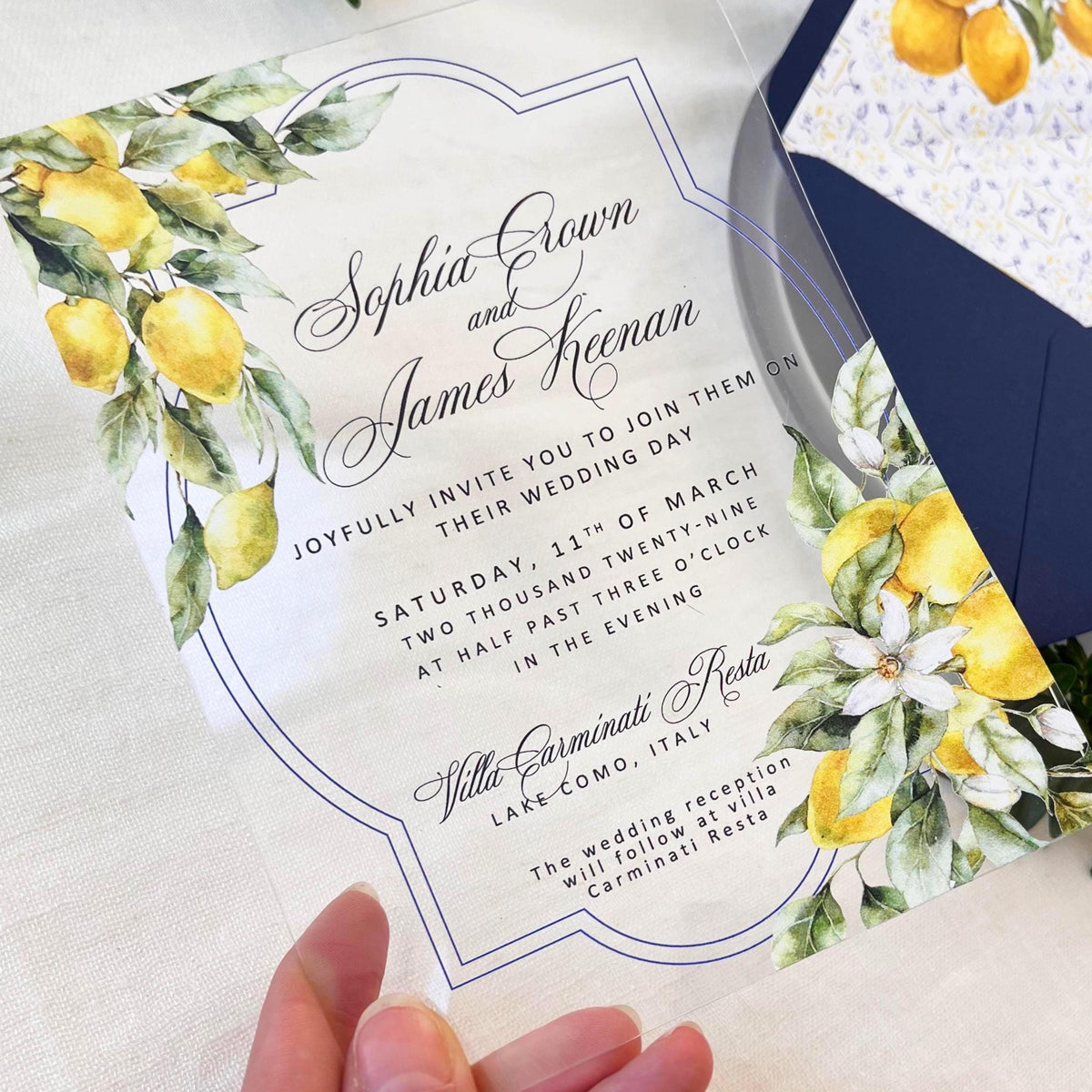 Transparent acrylic invitation with citrus design, accompanied by a blue envelope and decorative insert showcasing Santorini-inspired tiles and lemons.