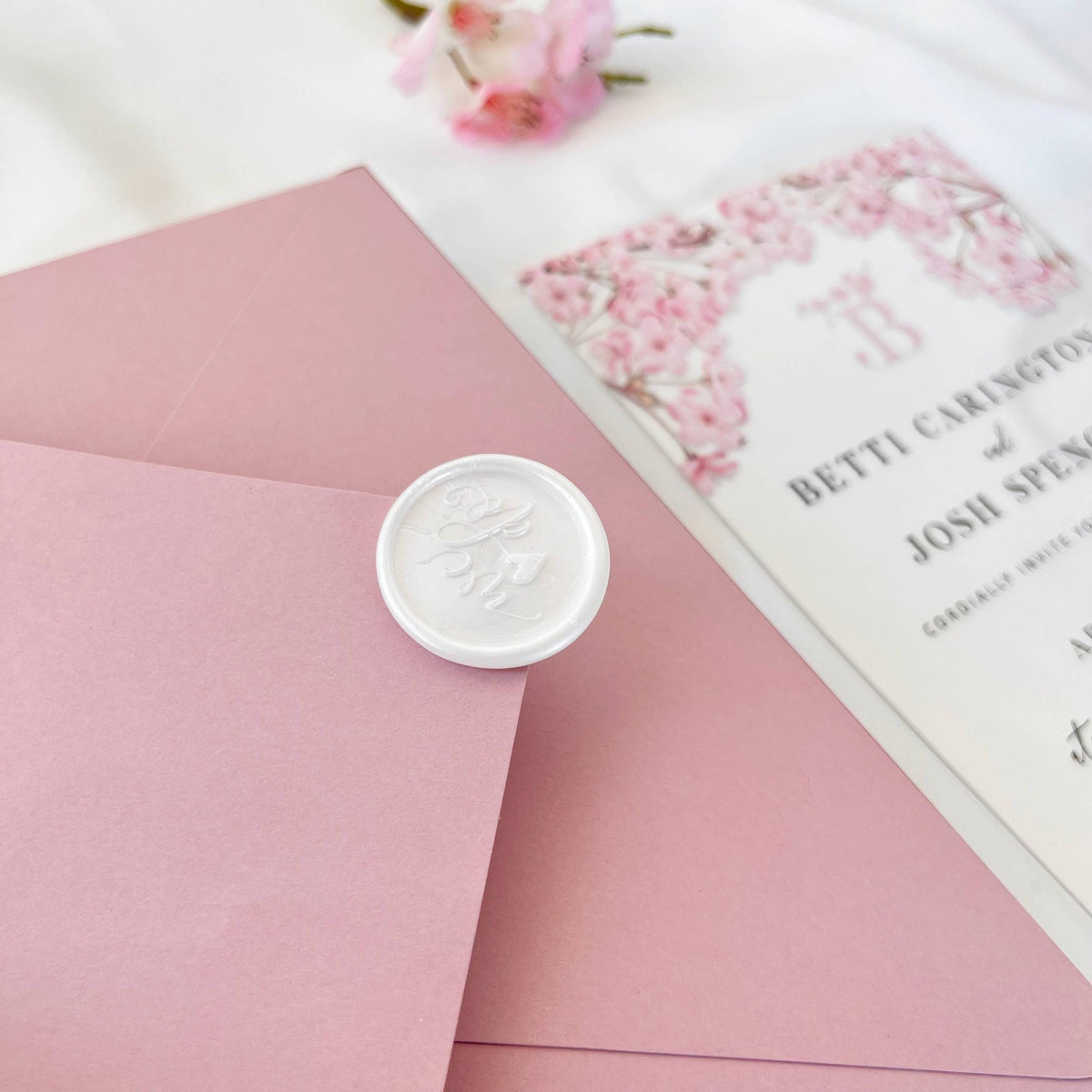 Luxury acrylic wedding invitation set with cherry blossom motif, blush envelope, and wax seal accent.