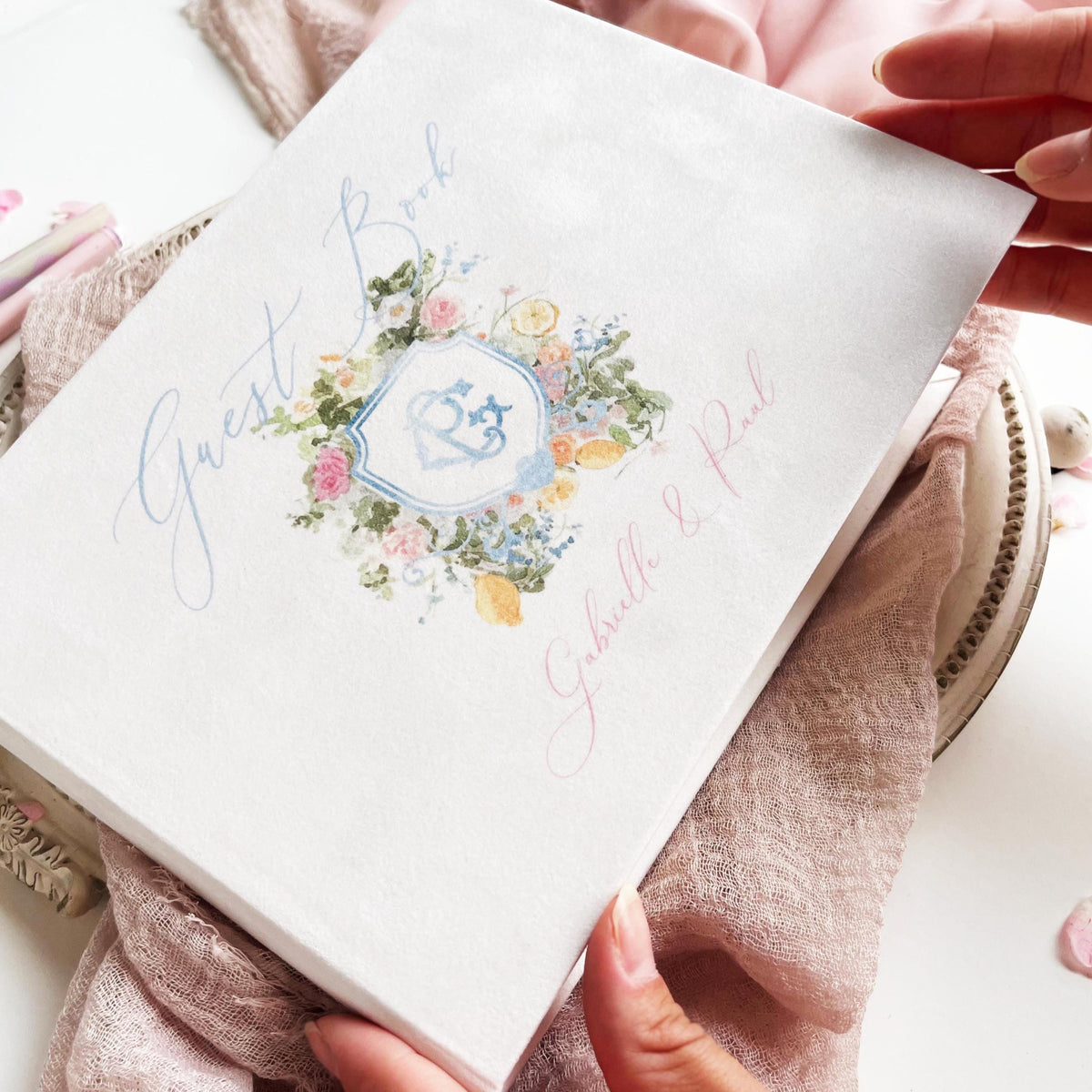 An elegant white velvet guest book designed with a personalized watercolor monogram of initials and floral motifs.
