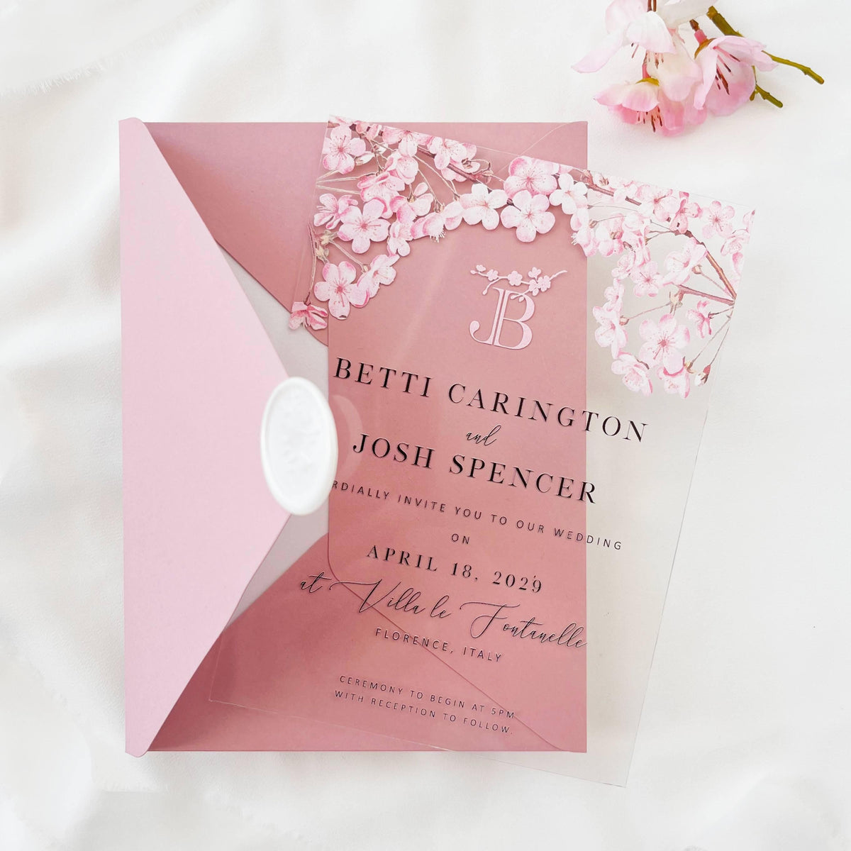 Elegant clear wedding invitation with sakura flowers, blush stationery, and metallic details.