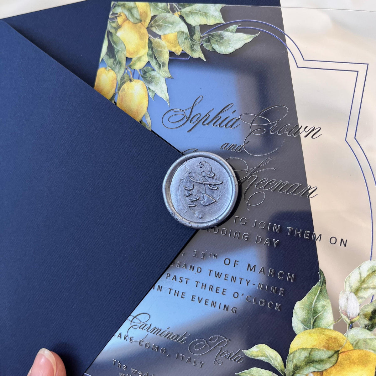 Elegant acrylic wedding invite with printed lemons, paired with a blue envelope, Santorini tile patterned insert, and a coordinating blue wax seal.