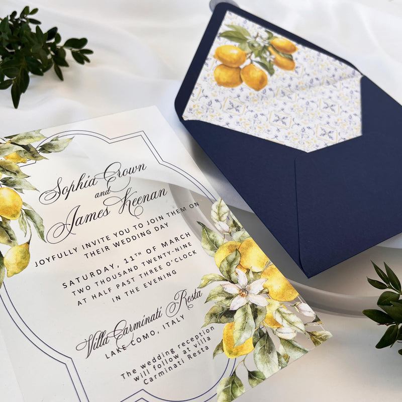 Clear acrylic wedding invitation featuring a lemon print, paired with a blue envelope containing an insert with Santorini tile and lemon motifs, finished with a blue wax seal reading “WE DO.”