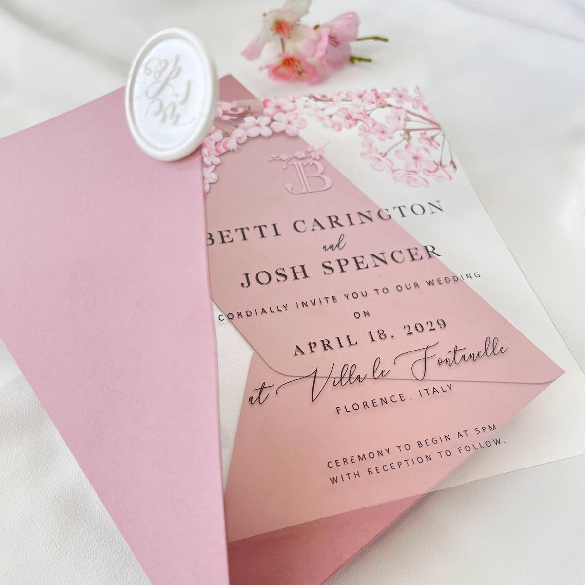 Transparent plexiglass wedding invite featuring soft pink cherry blossoms and elegant blush envelope.
