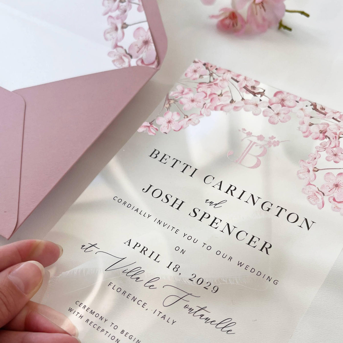 Elegant clear wedding invitation with sakura flowers, blush stationery, and metallic details.