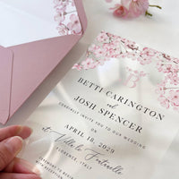 Elegant clear wedding invitation with sakura flowers, blush stationery, and metallic details.
