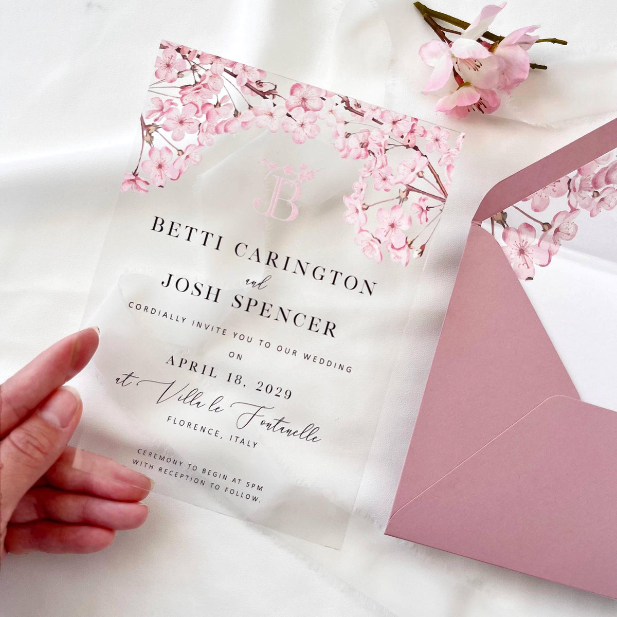 Luxury acrylic wedding invitation set with cherry blossom motif, blush envelope, and wax seal accent.
