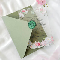 Transparent acrylic wedding invitation with printed rose design, sage green envelope, white liner, and monogram wax seal.