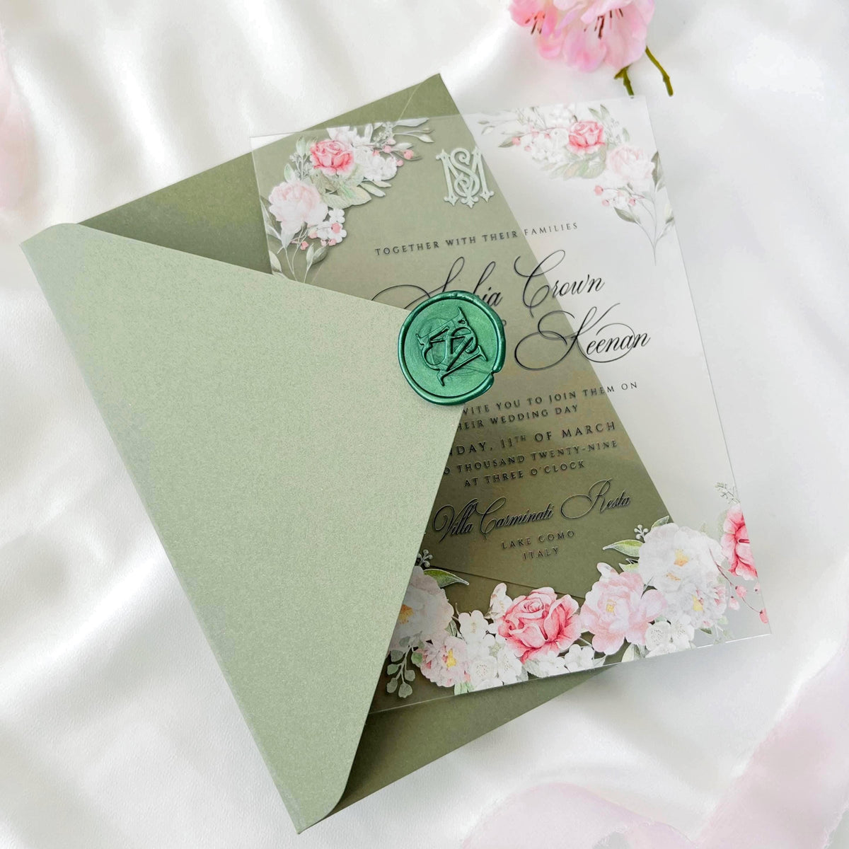 Transparent acrylic wedding invitation with printed rose design, sage green envelope, white liner, and monogram wax seal.
