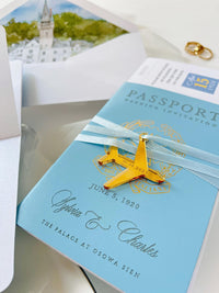 This wedding stationery suite features a blue faux leather passport invitation alongside a boarding pass RSVP card. The ensemble is completed by an elegant envelope lined with a custom watercolor illustration of the wedding venue's location.
